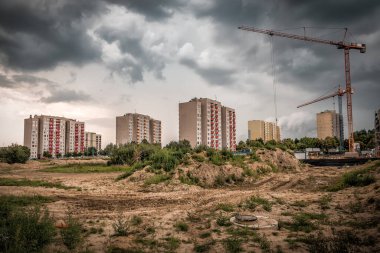 Çok katlı apartmanların ve fırtınalı bulutların altında çalışan vinçlerin inşaatı. Sanayi teması