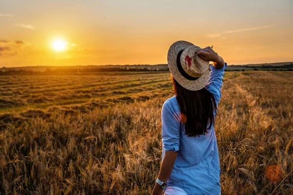 stock image Woman in straw hat looking forward to the sunset over a field of wheat