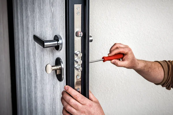 Professional handyman repair the door lock in metal entrance door, Man fixing lock with screwdriver