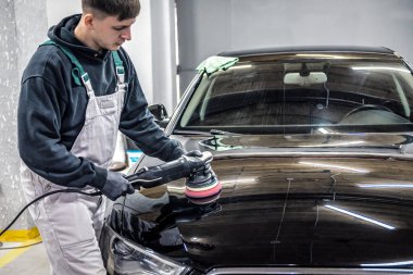 Araba temizliği ve cilalama konsepti. Profesyonel araba servisi çalışanı, yörünge cilası, beyaz lüks araba kaputunu cilalıyor. Sanayi teması