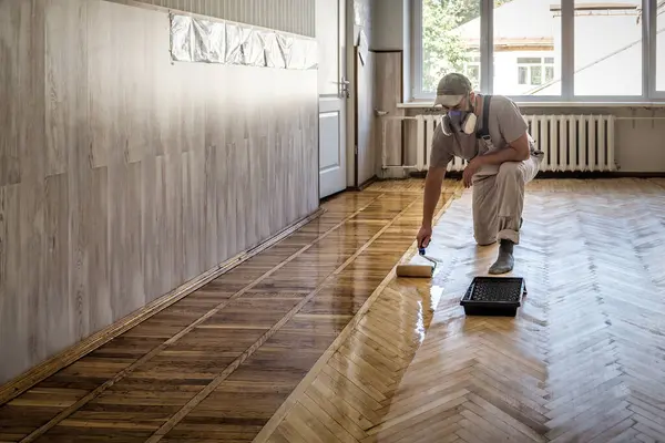 Worker uses a roller to coating floors. Varnishing lacquering parquet floor by paint roller. Industrial theme