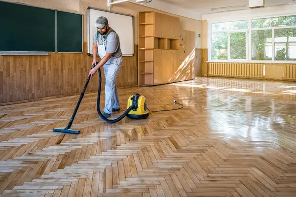 Worker carpenter cleans the lacquered parquet floor with professional vacuum cleaner. Industrial theme