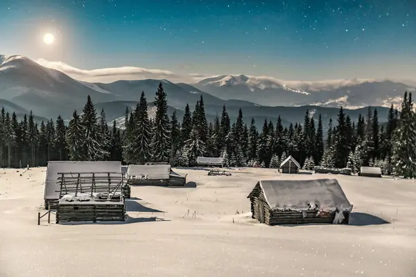 Abandoned village, wooden cabins in winter, snowy Carpathian mountains under moonlight