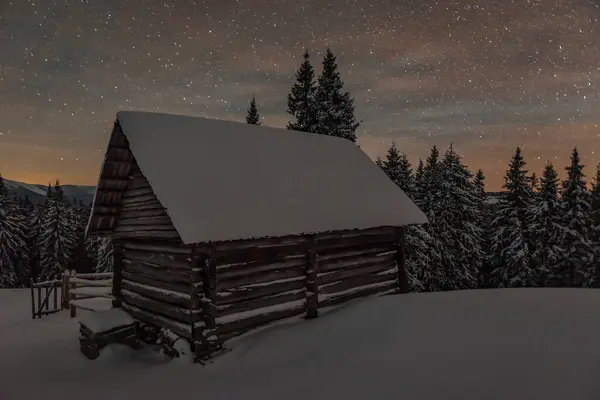Log wooden cabin hut under stars in winter snowy Carpathian mountains. Beautiful snowy landscape
