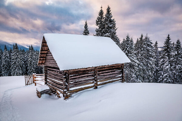 Wooden log cabin hut in snowy Carpathian mountains under cloudy sky