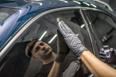 Adam arabanın camına nano koruyucu kaplama uyguluyor. Endüstriyel araba detay teması.