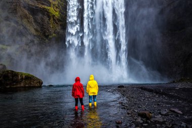 İzlanda 'da bulunan Skogafoss şelalesinin güzelliğine kırmızı ve sarı takdire şayan iki kişi. Seyahat teması