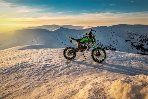Extreme cross sport motorcycle with chain on the wheels in winter snowy mountains at sunset or sunrise