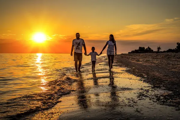 Silhouette of young family walking on the beach at sunset or sunrise. Family vacation theme