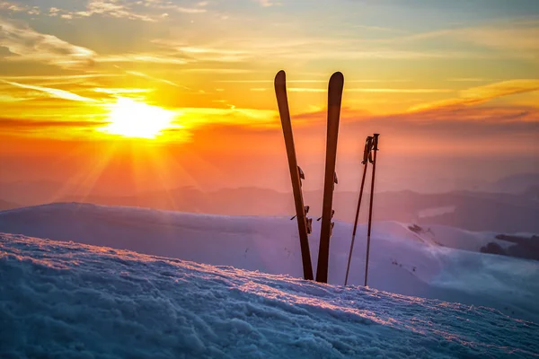 Ski and sticks on the snow in winter mountains at beautiful sunset or sunrise