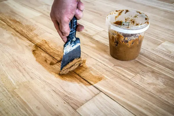 Carpenter fills the gaps cracks in the parquet with a spatula. Mixing retainer, varnish and a small mixture of wood. Industrial theme