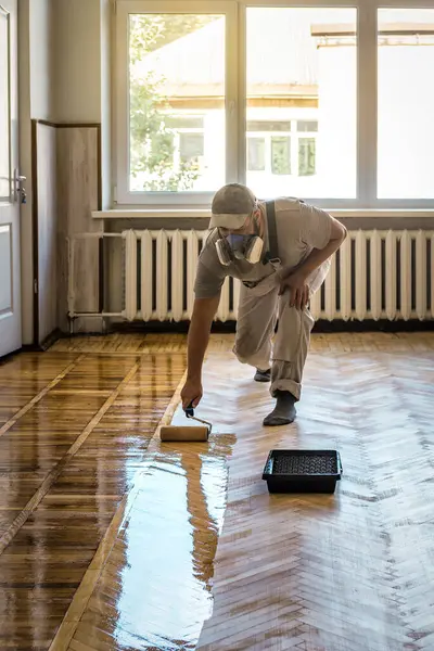 Renovation of old parquet floor, Worker varnishing wooden floor by paint roller. Industrial theme
