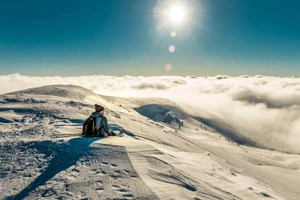Tourist hiker sitting on the snow in winter snowy Carpathian mountains under sunlight