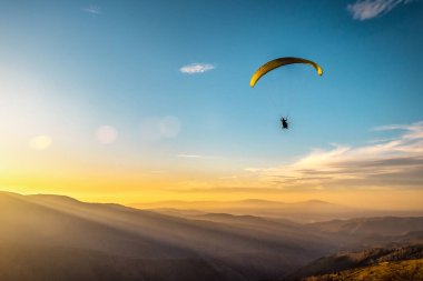 Paraglider silueti sisli dağ vadisinde güzel, ılık günbatımı ve gündoğumu renklerinde uçuyor.