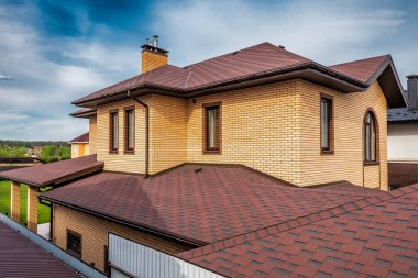 Güneşli bir günde modern çatılı, kahverengi kiremitli bir ev.