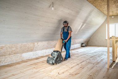 Profesyonel işçi mavi tulumlu, ahşap zemini öğütme makinesiyle temizliyor. Sanayi teması
