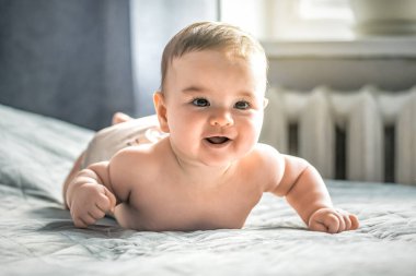 Evdeki bir yatakta güzel, sağlıklı, çıplak bir bebek yatıyor. Mutlu çocuk kameraya bakıyor.