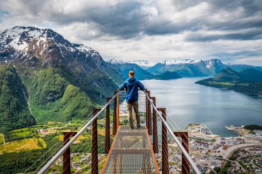 Man in blue standing on Rampestreken viewpoint over mountains in Norway. Travel and vacation theme clipart