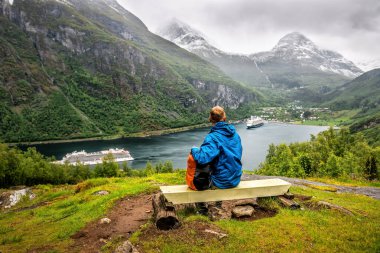 Mavi ceketli turist Geiranger fiyordunun üzerinde dinleniyor.
