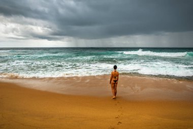 Kumsalda duran ve fırtınalı okyanusa bakan turist kadın.