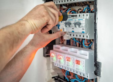 Tornavidayla çalışan profesyonel elektrikçinin elleri sigorta kutusundaki elektrikli aktivatör ekipmanlarını sıkılaştırıyor. Sanayi teması