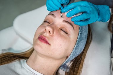 Güzellik salonunda mavi lastik eldivenli profesyonel kozmetik uzmanı cilt temizliği, sivilce sıkma yapıyor. SPA ve güzellik teması