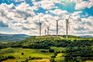 Rüzgar türbinleri ve güneş ışığı altında yeşil dağ manzarası. Yeşil enerji konsepti. Sanayi teması