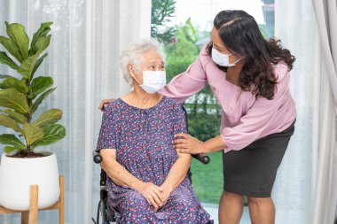 Bakıcı, Asyalı yaşlı ya da yaşlı kadın tekerlekli sandalyede oturan ve güvenlik enfeksiyonunu korumak için maske takan Covid19 Coronavirus 'a yardım ediyor..