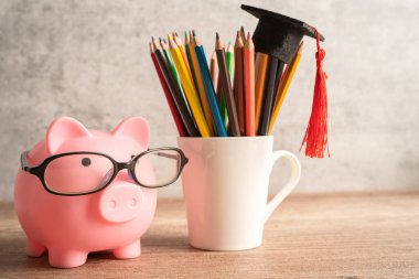 Pigging bank wearing eyeglass with colorful pencils; saving bank education concept.