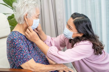 Bakıcı, parkta güvenlik enfeksiyonunu korumak için maske takan Asyalı yaşlı ya da yaşlı bir kadınla yardım ve sohbet eder..