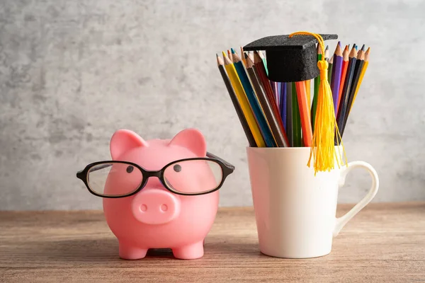 Pigging bank wearing eyeglass with colorful pencils; saving bank education concept.