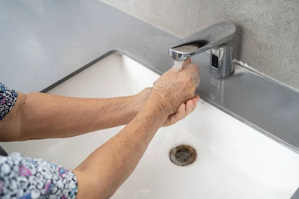 Asian senior or elderly old lady woman patient washing hand by soap and clean water for protect safety infection and kill Novel Coronavirus Covid-19 virus, bacteria and germs.