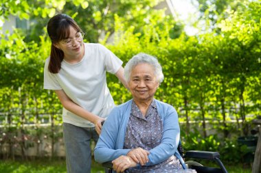 Caregiver help and care Asian elderly woman use walker with strong health while walking at park in happy fresh holiday.