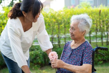 Caregive talk and help Asian elderly woman holding flower, smile and happy in the sunny garden.