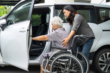 Caregiver help and support asian elderly woman sitting on wheelchair prepare get to her car to travel in holiday.