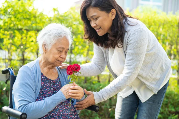 stock image Caregver help Asian elderly woman holding red rose flower, smile and happy in the sunny garden.