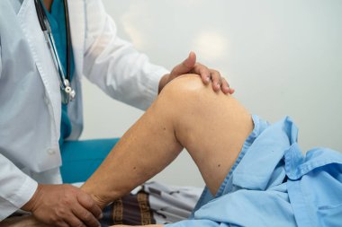 Ortopedi kliniğinde kıdemli bir hastanın diz ve bacağını muayene eden Asyalı doktor fizyoterapisti..