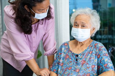 Tekerlekli sandalyedeki Asyalı yaşlı kadına yardım eden ve güvenlik enfeksiyonunu korumak için maske takan bakıcı Covid19 Coronavirus.