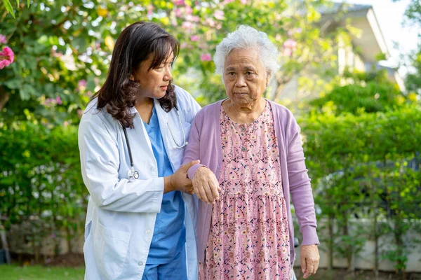 Doctor caregiver help and care Asian senior woman patient walking in park at hospital.