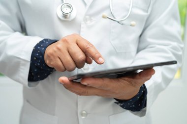 Asyalı akıllı doktor elinde dijital tablet teknolojisi ile hastanedeki hastaların tedavi yöntemlerini araştırıyor..