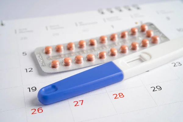 Pregnancy test and birth control pills on calendar, contraception health and medicine.