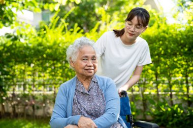 Caregiver help and care Asian elderly woman use walker with strong health while walking at park in happy fresh holiday.