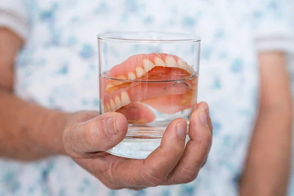 亚洲老年妇女 因咀嚼良好而将假牙握在水清洁剂杯中清洗 — 图库照片