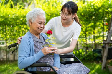 Asian elderly woman holding red rose flower, smile and happy in the sunny garden.