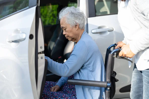 stock image Caregiver help and support asian elderly woman sitting on wheelchair prepare get to her car to travel in holiday.