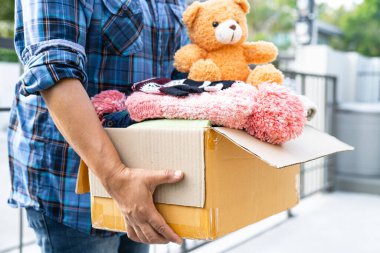 Volunteer woman provide clothing donation box with used clothes and doll to support help for refugee, homeless or poor people in the world.