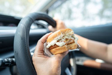 Arabada yemek için hamburger tutan Asyalı kadın tehlikeli ve kaza riski taşıyor..