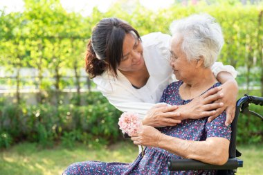 Caregive talk and help Asian elderly woman holding flower, smile and happy in the sunny garden.