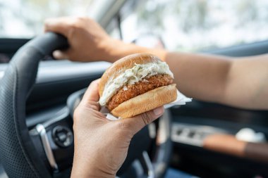 Arabada yemek için hamburger tutan Asyalı kadın tehlikeli ve kaza riski taşıyor..