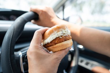 Arabada yemek için hamburger tutan Asyalı kadın tehlikeli ve kaza riski taşıyor..